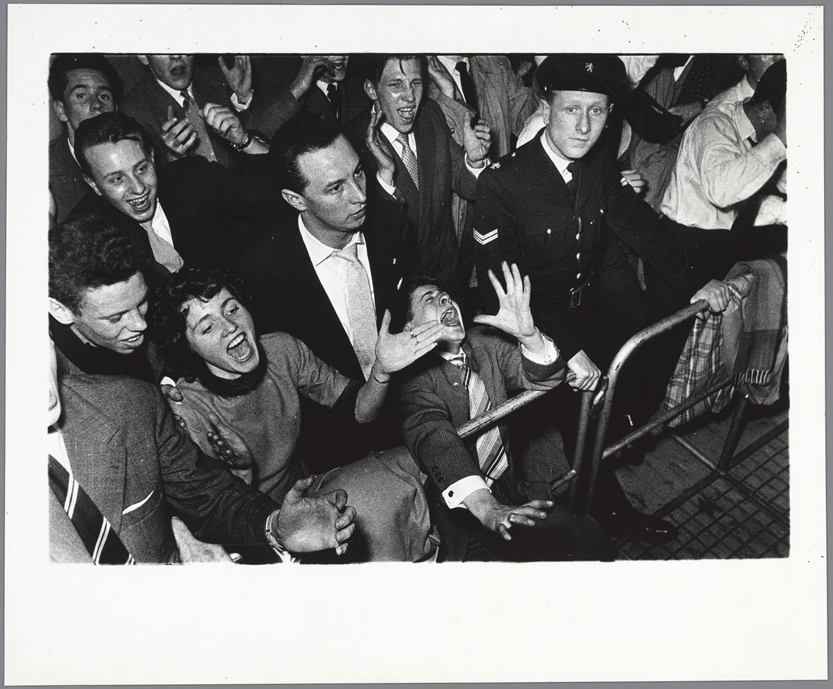 Ed van der Elsken, Concertbezoekers en een agent achter dranghekken bij een concert van de Lionel Hampton Big Band in de Houtrusthallen in Den Haag, 24 maart 1956, ontwikkelgelatinezilverdruk/ gelatin silver print
