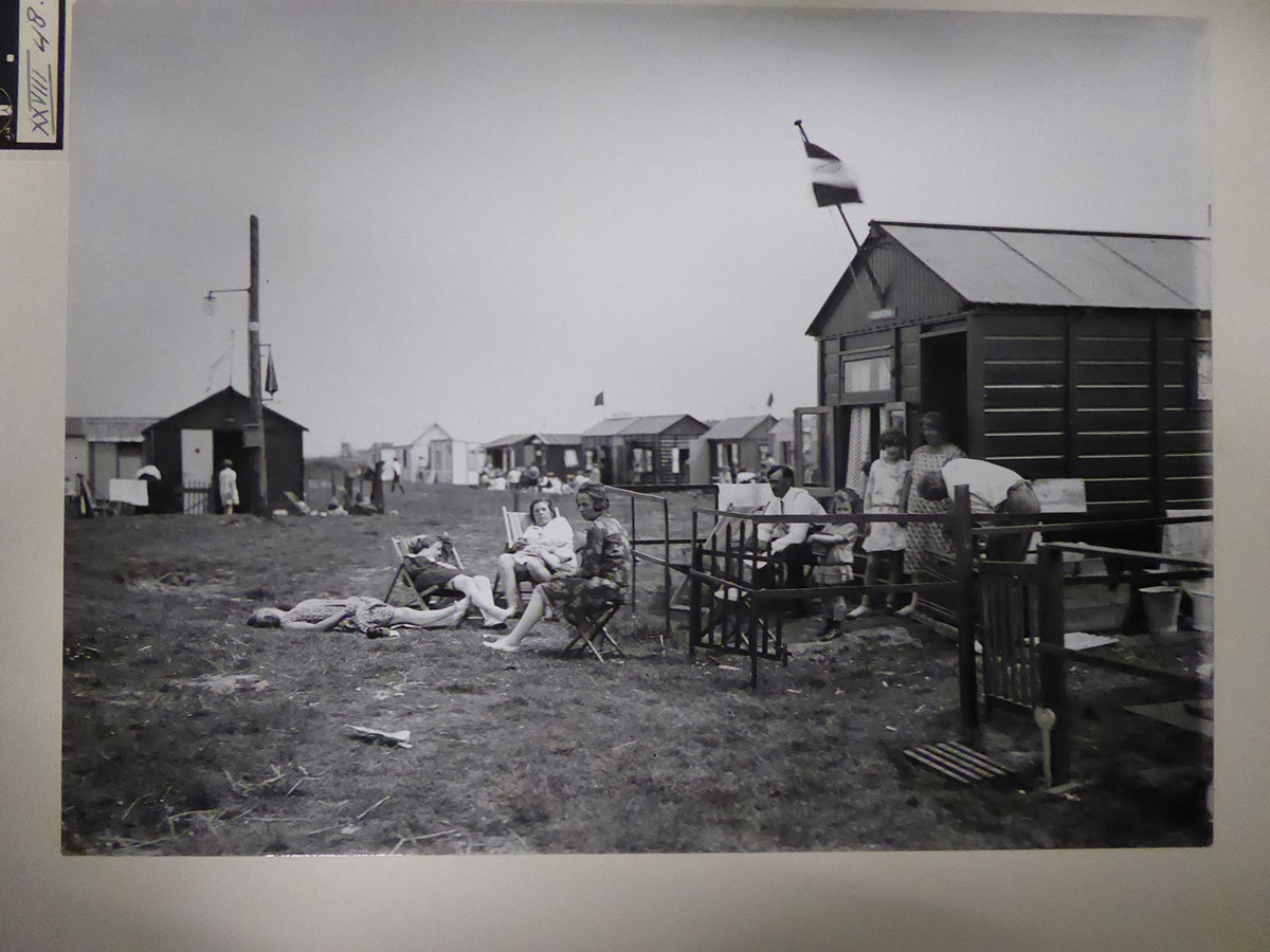 Gemeentelijk Kampeerterrein, Schelpweg, 1930<br>
Adriaan van Agtmaal (1887-1960) / collectie Stadsarchief Rotterdam / P. Houwer-van Agtmaal
In 1930 fotografeerde Van Agtmaal uit Baarn het Gemeentelijk Kampeerterrein aan de Schelpweg achter de duinen. Vermoedelijk in opdracht van de Gemeentelijke Strandcommissie die zich intensief met de ontwikkeling van Hoek van Holland als badplaats bezighield.<br>
In 1923 was de opening van het kampeerterrein. Door de snelle toename van het aantal huisjes veranderde het complex al snel in een huisjespark. Het werd hierdoor zowel het eerste officiële seizoenskampeerterrein als het oudste vakantiepark van Nederland. De 'houten kampeerstad van Rotterdam aan zee' telt intussen 900 huisjes en heet nu Recreatieoord Hoek van Holland.