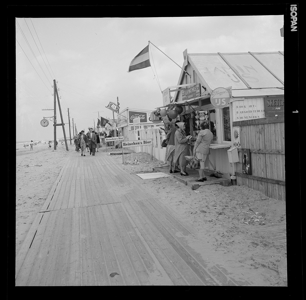 Strand, Hoek van Holland, 1957<br>
Jan Roovers (1912-2000) / collectie Henk van der Lugt<br>
Jan Roovers fotografeerde, heel nauwgezet, van 1945 tot 1965 de veranderende straten van Rotterdam. Als een archeoloog volgde hij hoe Rotterdam een nieuw aanzien kreeg. Met nieuwe brede wegen, moderne hoogbouw in het centrum en nieuwe wijken in de polders rondom. Op veel opnamen staan bladerloze bomen. Die foto's verkocht hij aan het Stadsarchief Rotterdam. Soms maakte hij opnamen van bomen in vol blad, dat werden dan ansichtkaarten. Deze topografische foto's waren voor hem een 'stopklus', voor wanneer hij zonder betaalde opdrachten zat. Hij kwam ook regelmatig in Hoek van Holland, op het strand en ook op De Beer.