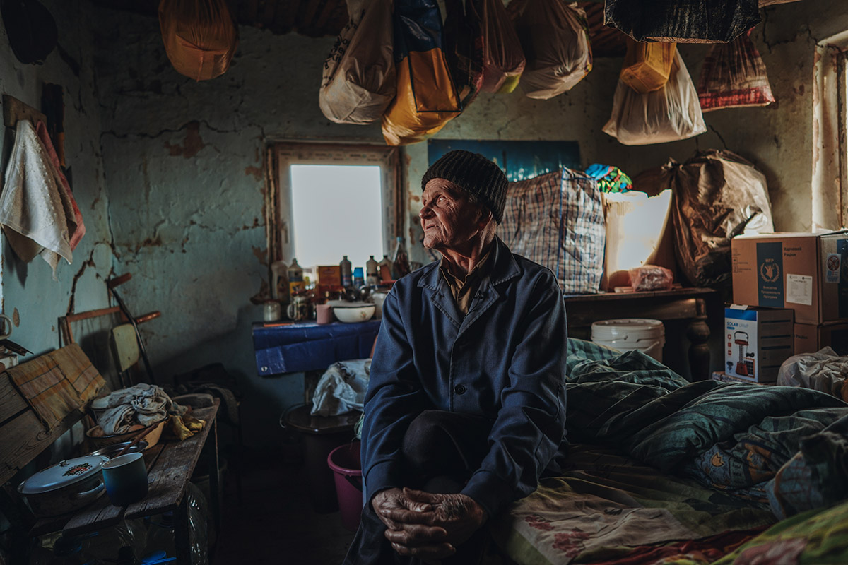 Yarosjenko Viktor Petrovych, Cherson, Oekraïne<br>
Lieuwe Siebe de Jong - 2024<br>
Yarosjenko Viktor Petrovych zit in het pand naast zijn huis, dat gebruikt wordt als zomerkeuken. Hij wordt nu gedwongen daar te wonen, omdat zijn huis verwoest is. Acht maanden lang leefde hij onder de bezetting van de Russen. Zijn dochter stierf in de strijd in Bakhmut. Yarosjenko probeerde zich in te schrijven voor het leger, maar werd afgewezen. 'Ik wou dat ik de plaats van mijn dochter kon innemen en in de strijd kon sneuvelen', zegt hij.