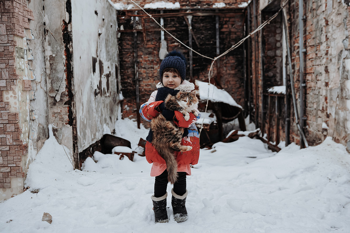 Anya, Tsjernihiv, Oekraïne<br>
Lieuwe Siebe de Jong - 2022<br>
Anya poseert met haar kat in wat ooit haar slaapkamer was. In het begin van de oorlog vielen de Russen haar dorp aan. Op de grond ligt een rakethuls, groter dan haar lichaam, die het hele huis verwoestte. Gelukkig schuilde ze tijdens de bombardementen in de kelder van de buren. ZOA gaf geld aan haar ouders, zodat ze een nieuw onderkomen konden bouwen.