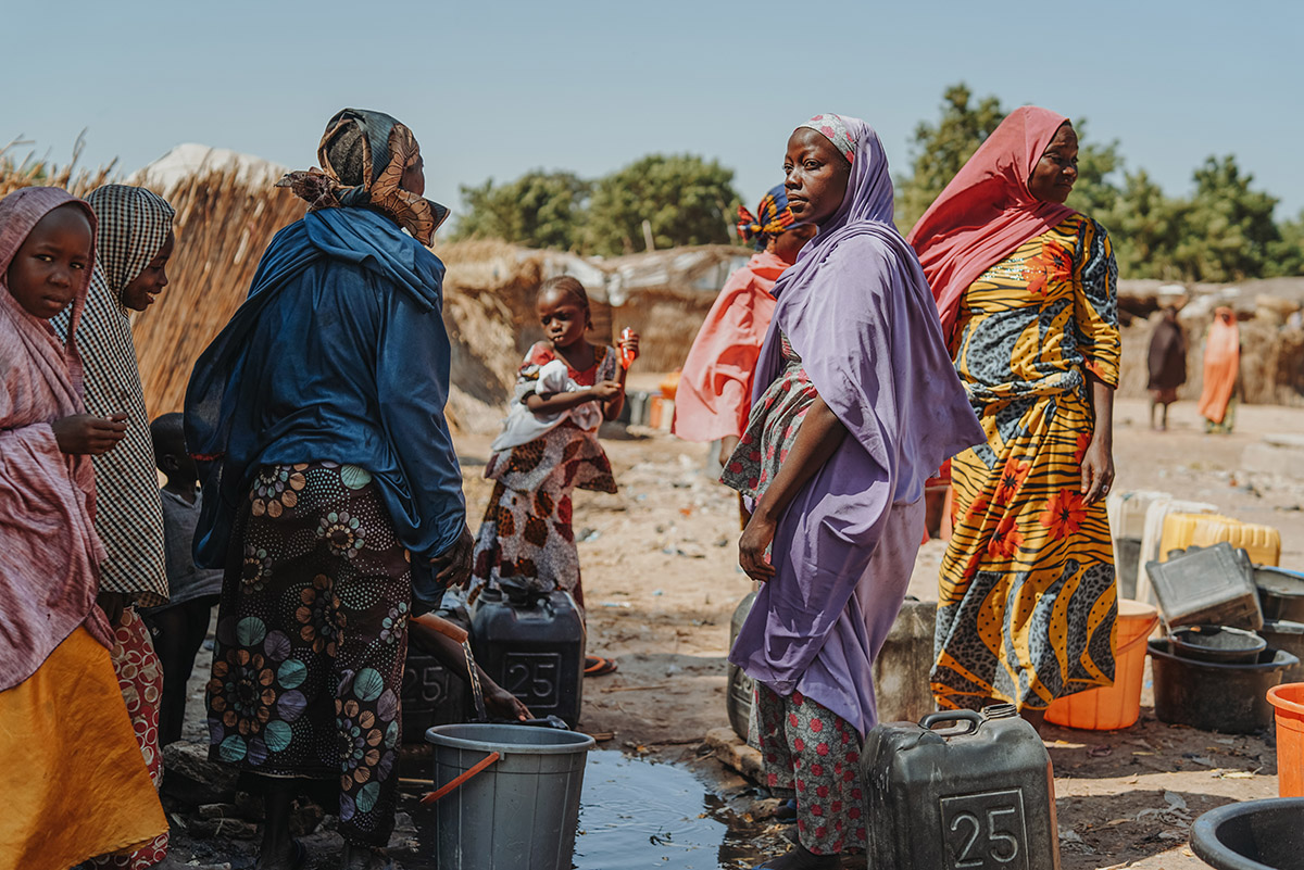 Habiba, Borno, Nigeria<br>
Lieuwe Siebe de Jong - 2021<br>
Habiba (in het paars) moest geboorteplaats te ontvluchten vanwege aanvallen van terreurorganisatie Boko Haram. Met haar man en vier kinderen bereikte ze veilig het vluchtelingenkamp Gongulong. Toen haar man later terugkeerde naar hun rijstveld om te oogsten, werd hij onthoofd. Habiba heeft nu geen enkele bron van inkomsten meer. ZOA gaf haar zaden om een eigen moestuin te beginnen. Daarnaast bouwde ZOA watertorens en latrines om schoon water en hygiëne te bieden aan de vele vluchtelingen in het kamp.
